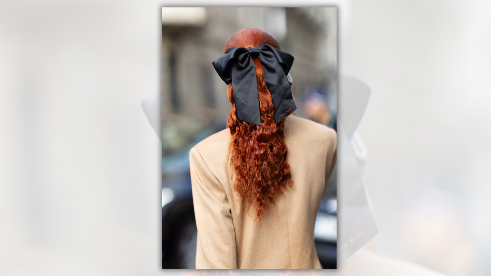 A person with red hair wearing a black bow and cream top is photographed from the back.